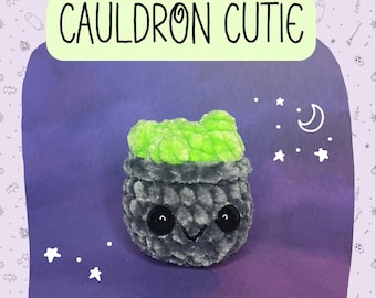Puede incluir: Un caldero gris con una parte superior verde y ojos negros. El caldero es un juguete de peluche con una expresión linda. El fondo es un degradado morado con estrellas blancas.