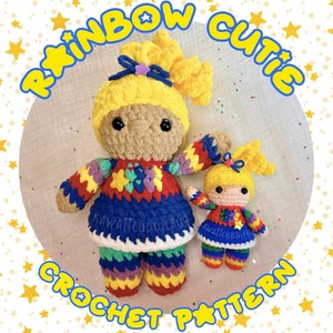 May include: Rainbow Cutie Crochet Pattern featuring two crocheted dolls. The larger doll is wearing a rainbow patchwork dress and the smaller doll is wearing a similar dress. Both dolls have yellow hair and black eyes.