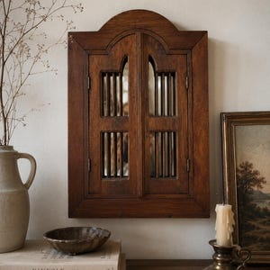 May include: A dark brown wooden wall mirror featuring two hinged shutter doors with vertical slats and an arched top design. The mirror frame has a rectangular shape with a curved upper edge, showcasing a natural wood grain finish.