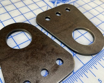 May include: Two metal brackets with rounded edges and multiple holes. The brackets are a dark brown color and have a rough, textured surface.