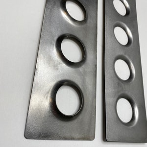 Op de afbeelding: Twee rechthoekige metalen platen met afgeronde gaten. De platen hebben een doffe zilveren kleur en een geborstelde textuur. Een liniaal met inch-maten staat onderaan. De platen zijn ongeveer 15 cm lang.