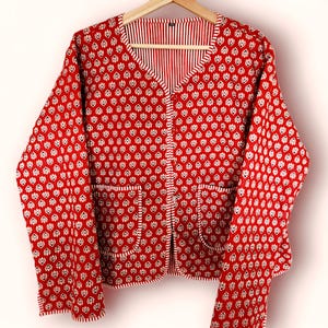 May include: A red and white patterned cardigan with a button closure and two pockets. The cardigan has a V-neck and long sleeves.