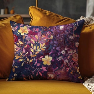 May include: A throw pillow with a floral pattern featuring purple, pink, yellow, and white flowers on a dark blue background. The pillow is on a mustard yellow sofa.