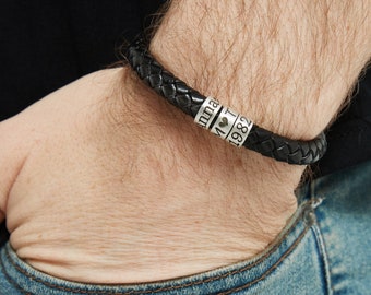 Può includere: Un braccialetto intrecciato in pelle nera con perline d'argento. Le perline sono incise con il testo "Anna", un simbolo di cuore, "1" e "1982".