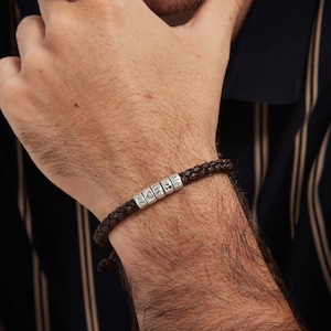 May include: A brown leather bracelet with silver beads that spell out "Alex & Lisa" and a heart symbol. The bracelet also includes the year "1993".