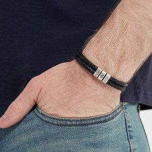 May include: A black leather bracelet with two strands and silver metal beads. The beads are engraved with the names "Elmore" and "Kelly" and an ampersand symbol.