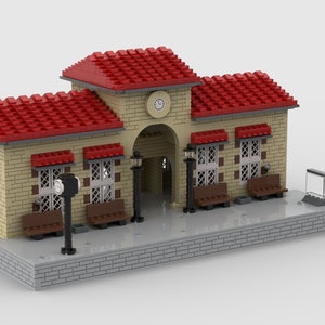 Könnte beinhalten: Ein Lego-Modell eines Bahnhofs mit einem roten Ziegeldach, Backsteinwänden und einer Uhr an der Vorderseite. Auf dem Bahnsteig befinden sich Bänke und ein Laternenpfahl.