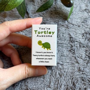 May include: A small white card with the text "You're Turtley Awesome" in green and a cartoon turtle illustration. The card also includes the text "I know it, you know it. Teeny turtle is always here, whenever you need a little cheer."