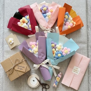 May include: Five crochet flower bouquets wrapped in colorful paper with white ribbons, a brown gift box with a 'Handmade for You' tag, a small card with a crochet flower, a spool of ribbon, scissors, a glass vial of tiny flowers, and a pink gift package.