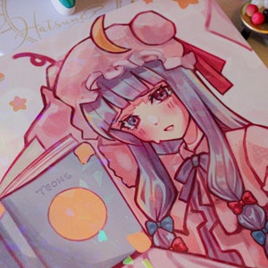 Könnte beinhalten: Eine Zeichnung, die einen rosa und blauen Anime-Charakter mit langen blauen Haaren zeigt. Sie trägt ein rosa Kleid mit einem weißen Kragen und einen rosa Hut mit einem Halbmond oben drauf. Sie hält ein Buch mit dem Wort "TEONS" auf dem Cover. Der Hintergrund ist hellrosa mit weißen Sternen.