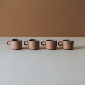 Row of small terracotta ceramic cups with ring handles in neutral earthy tones