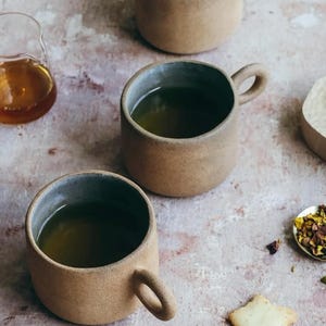 Top view of two terracotta ceramic cups filled with tea on textured table surface