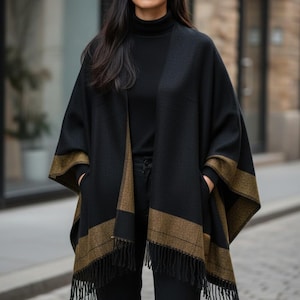 May include: A black cape with gold trim and fringe. The cape is worn over a black turtleneck and black trousers. The cape has a rectangular gold band near the bottom and on the sleeves.