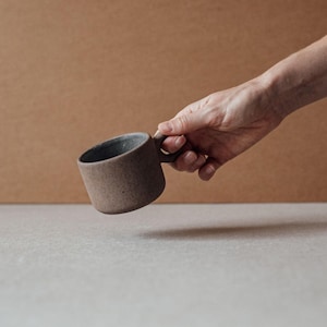 Hand holding a small terracotta ceramic mug with sculptural ring handle