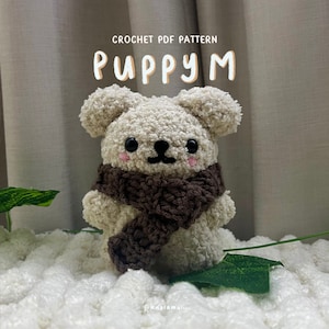 May include: Crochet PDF pattern for a cute, white, fluffy puppy wearing a brown scarf. The pattern is called "Puppy M".