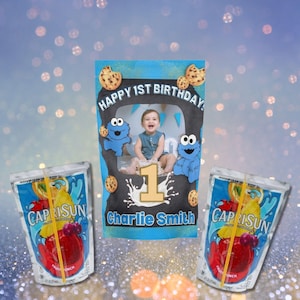 May include: A custom birthday photo prop featuring a child's photo, Cookie Monster, and chocolate chip cookies. The text reads "Happy 1st Birthday" and "Charlie Smith." Two Capri Sun juice pouches are also visible.