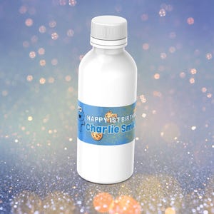 May include: A white bottle with a blue label featuring Cookie Monster and the text "HAPPY 1ST BIRTHDAY Charlie Smith" with cookie illustrations. The bottle has a white cap and is set against a blurred, glittery background.