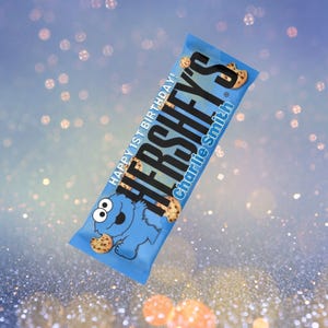 May include: A blue Hershey's candy bar wrapper featuring a cartoon character and the text "HAPPY 1ST BIRTHDAY!" and "Charlie Smith". The wrapper has a cookie theme.