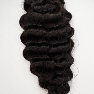 May include: A bundle of dark brown human hair extensions with loose waves. The hair is tied together with gold wire.