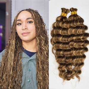 May include: Two bundles of wavy brown and blonde human hair extensions. The hair is tied together with gold bands.