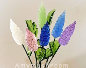 Puede incluir: Un ramo de seis flores de vidrio en un jarrón de vidrio transparente. Las flores son en tonos de blanco, rosa, verde, azul y morado. Las flores están dispuestas en un jarrón con una superficie texturizada.