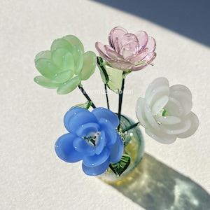 May include: A glass vase filled with four glass flowers. The flowers are green, pink, blue, and white.