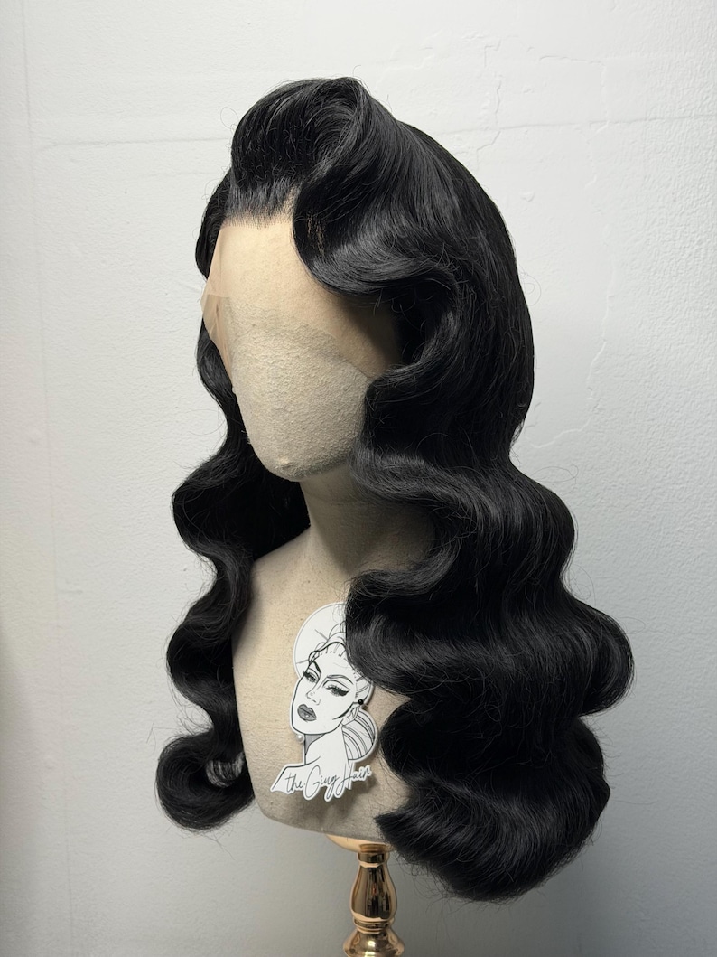 May include: A black, vintage-style wig with long, wavy curls. The wig is styled with a side part and features a natural-looking hairline. The wig is displayed on a mannequin head with a sticker that says "The Guy Hair".
