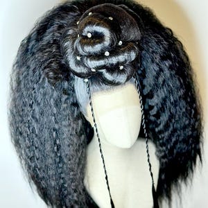 Könnte beinhalten: Eine schwarze Perücke mit langen, lockigen Haaren und einem Dutt oben. Der Dutt ist mit silbernen Strasssteinen verziert. Die Perücke sitzt auf einem Mannequin-Kopf.