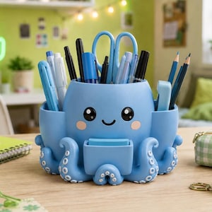 May include: A light blue octopus-shaped desk organizer featuring a smiling face with large black eyes and pink cheeks. The container has multiple compartments holding various pens, pencils, scissors, and a small stack of blue sticky notes.