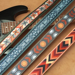 May include: Four guitar straps with different colorful patterns. The straps are made of fabric and have a woven design. The straps are laid out on a brown surface.