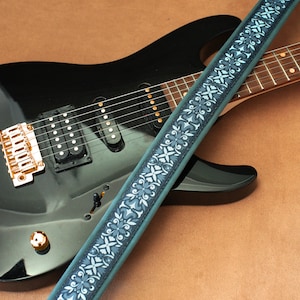 May include: A black electric guitar with a gold-colored bridge and a blue and white patterned guitar strap.