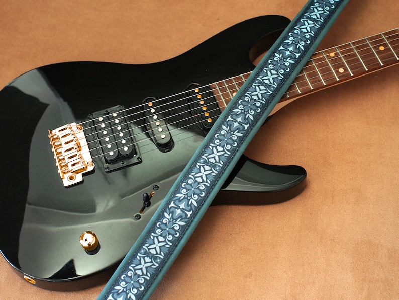 May include: A black electric guitar with a gold-colored bridge and a blue and white patterned guitar strap.