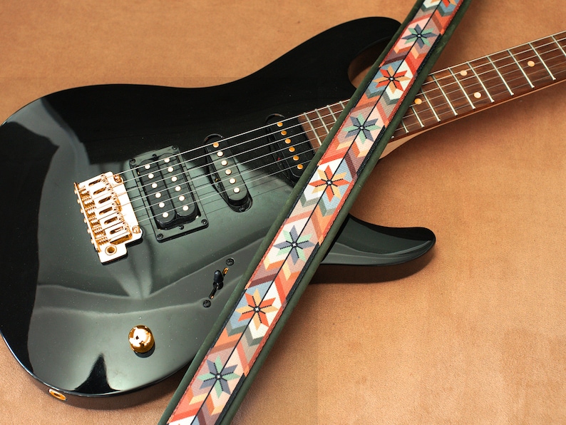 May include: A black electric guitar with a gold-colored bridge and a colorful patterned guitar strap.