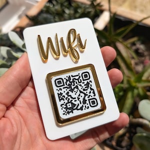 May include: White sign with gold lettering that says "Wifi" and a gold framed black and white QR code.