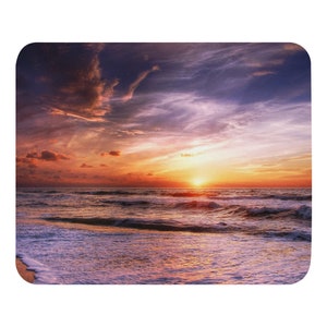 Könnte beinhalten: Ein lebendiger Sonnenuntergang über einem ruhigen Meer mit Wellen, die sanft an das Ufer schlagen. Der Himmel ist ein Mix aus orange, rosa und violetten Farbtönen, wobei die Wolken das warme Licht reflektieren.
