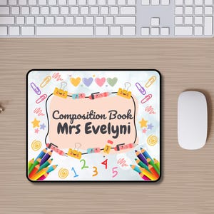 Pode incluir: Um mousepad retangular com uma borda preta, com um fundo azul claro e ilustra&ccedil;&otilde;es coloridas. O mousepad tem o texto "Composition Book Mrs Evelyni" no centro, rodeado por l&aacute;pis, clipes de papel e cora&ccedil;&otilde;es.