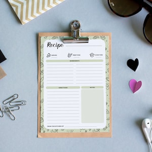 Puede incluir: Una plantilla de receta blanca con un borde verde y un respaldo de papel marr&oacute;n. La plantilla tiene secciones para "Sirve", "Tiempo de preparaci&oacute;n", "Tiempo de cocci&oacute;n", "Ingredientes", "Instrucciones" y "Notas". La plantilla est&aacute; en un portapapeles con un clip plateado.