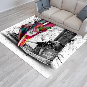 May include: A white and black area rug with a graphic design of two sneakers. One sneaker is red, pink, blue, and green. The other sneaker is white with black accents. The sneakers are covered in graffiti-style lettering.