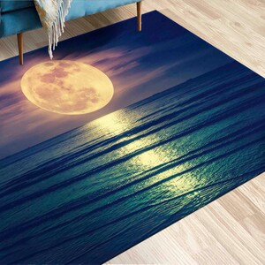 May include: A blue and green rug with a large, yellow moon and a rippling ocean scene. The rug has a soft, textured surface.