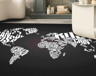 May include: Black area rug featuring a world map design. The map is composed of white text, with country names forming the continents. The rug is placed on a light-colored floor, with a white chair and table in the background.