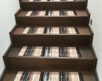 May include: Stair treads with a vertical striped pattern in black, white, and tan. The treads are placed on dark brown wooden stairs, creating a contrasting design element. The treads add a decorative and functional touch to the staircase.