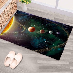 Può includere: Un tappeto rettangolare con una vivace raffigurazione del sistema solare su uno sfondo spaziale stellato, verde scuro e blu. Il design include il sole, i pianeti e le cinture di asteroidi. Il tappeto è posizionato su un pavimento in legno chiaro.