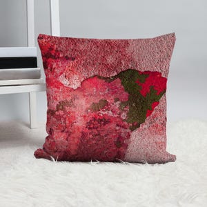 May include: Red, pink, and brown abstract throw pillow with a textured, distressed look. The pillow has a faded, vintage aesthetic.