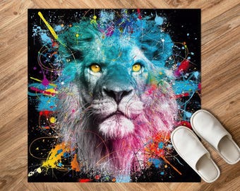 May include: A vibrant lion art print featuring a teal mane and yellow eyes. The lion's face is central, surrounded by colourful paint splatters in blue, pink, yellow, and red. Two white slippers are placed on the wooden floor.
