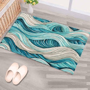 Peut inclure: Un tapis de sol rectangulaire avec un motif de vagues dans des tons de bleu, turquoise et beige. Le design évoque l'eau qui coule. Le tapis est posé sur un sol en bois gris clair, avec des pantoufles blanches à proximité.