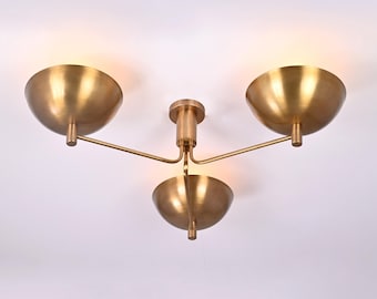 May include: A brass ceiling light fixture with three round shades. The shades are angled downwards and have a smooth, polished finish.