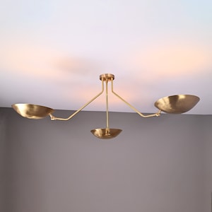 May include: A gold-toned ceiling light fixture with three adjustable arms and bowl-shaped shades.