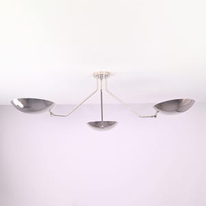 May include: A contemporary ceiling light fitting featuring three polished metal bowl-shaped shades. The fitting has a central stem with two arms extending outwards, each holding a shade. The shades are angled downwards.