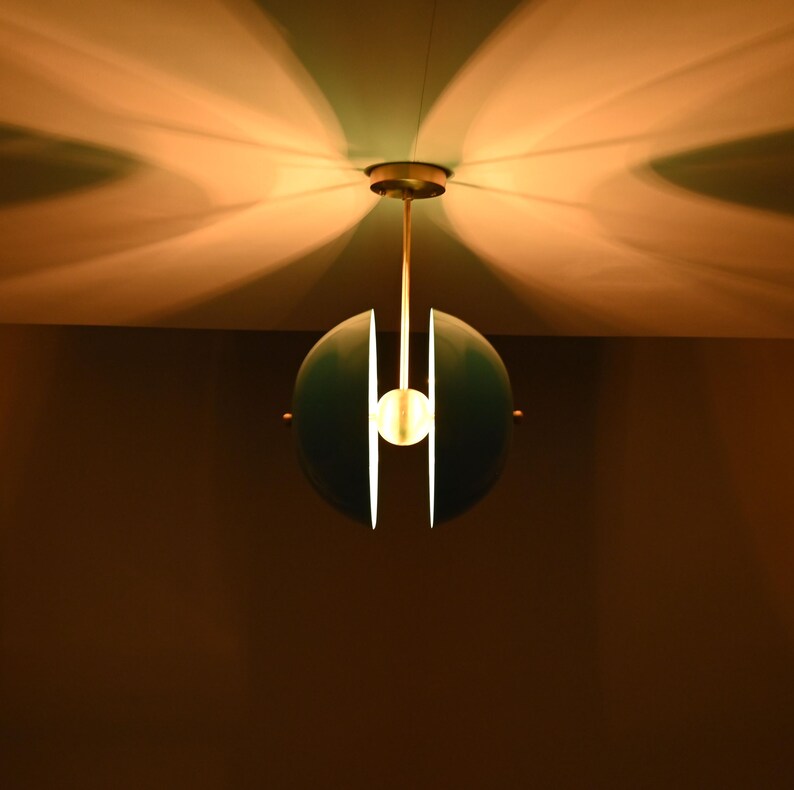 Op de afbeelding: Een tealblauwe globe hanglamp met een wit centrum en een enkele gloeilamp erin. De lamp hangt aan een plafond met een witte en lichtbruine achtergrond.