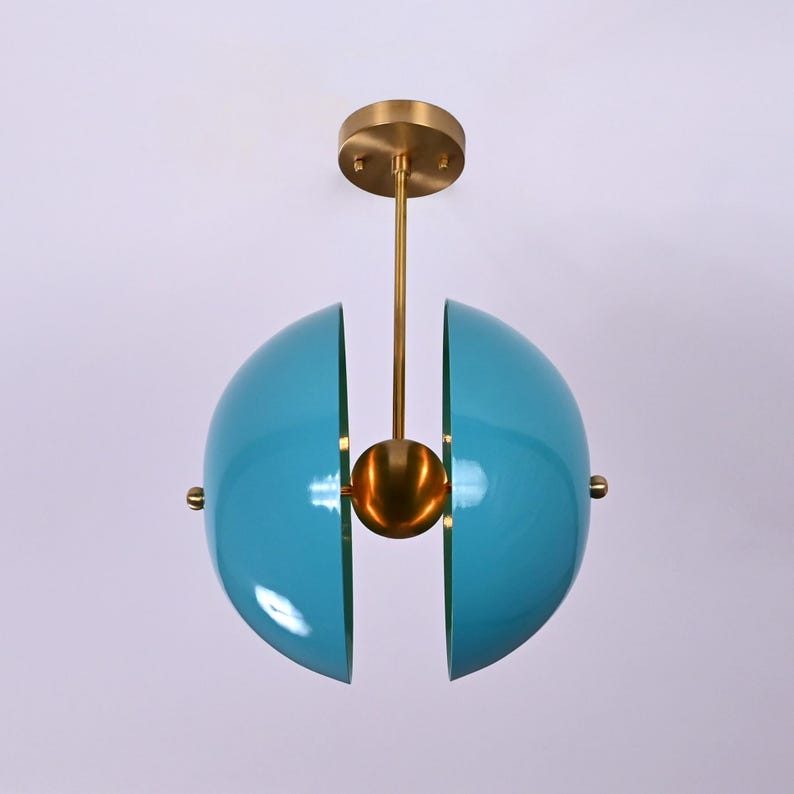 Op de afbeelding: Een moderne plafondlamp met twee blauwe halfronden die opengaan om een ​​gouden bol in het midden te onthullen. De lamp is opgehangen aan een gouden stang.